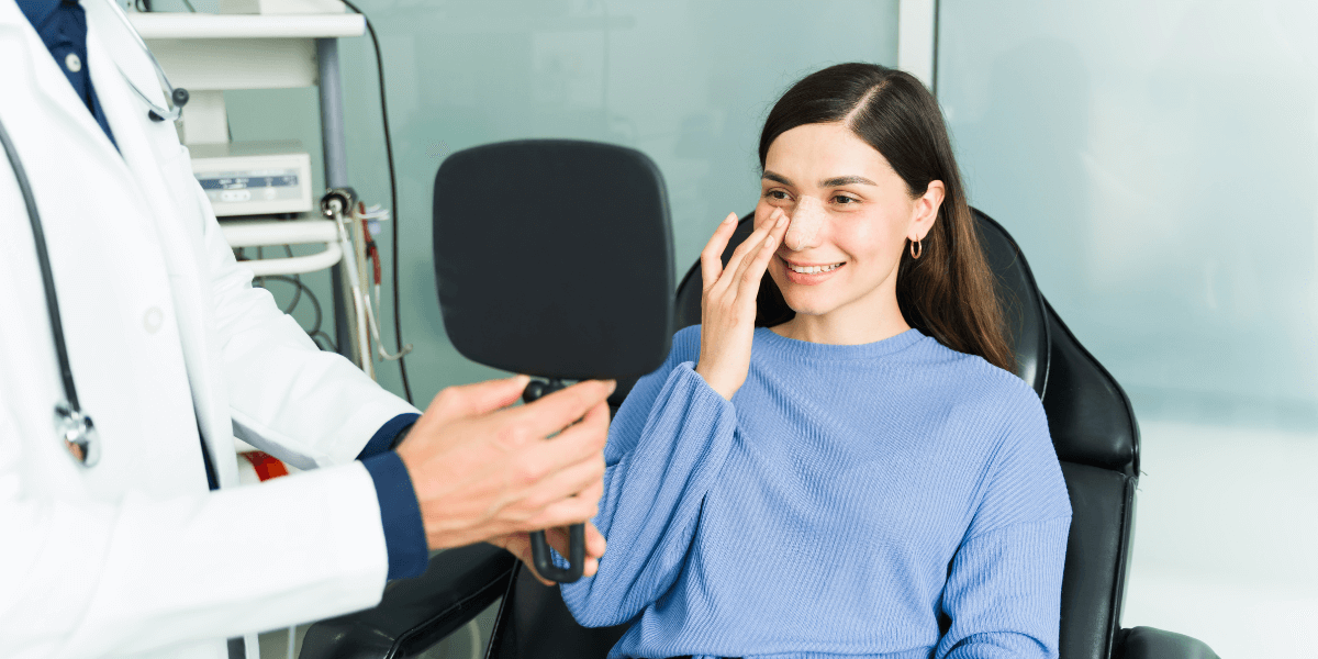 Young woman in a chair looking into a hand mirror that her doctor is holding.